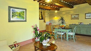 Un'area pranzo con un tavolo e sedie in legno, una cucina sullo sfondo e un tavolo da pranzo con un vaso di fiori.