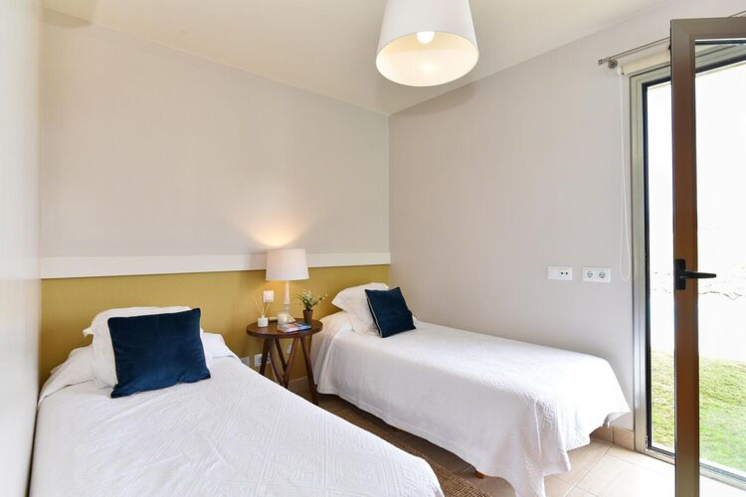 Hotellihuone, jossa on kaksi erillistä sänkyä, yöpöytä lampun kanssa ja näkymä lasiovesta.