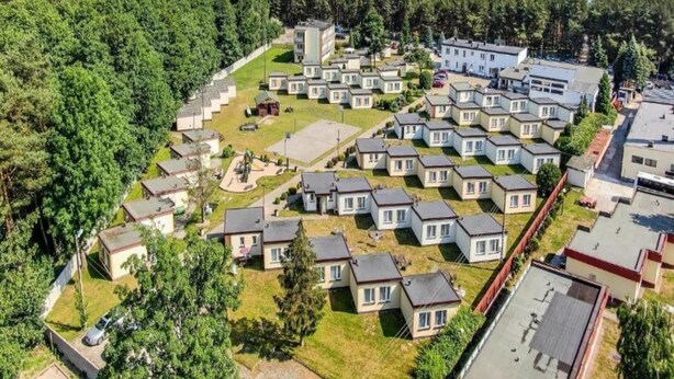 An aerial view of a residential area with multiple single-story houses, a central open space, and a dense forest in the background. - Single-story Holiday Homes Very Close to the Beach (gmina Sianów)
