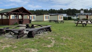 A campground with wooden picnic tables, a covered barbecue area, and small cabins with attached porches. - Single-story Holiday Homes Very Close to the Beach (gmina Sianów)