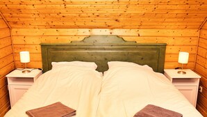 A wooden cabin room with a bed, two nightstands, and lamps.