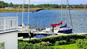 A marina with boats docked, a white building with a balcony, and a green landscape in the background. - Doppelhaushalfte, Ostseeresort Olpenitz (Kappeln)