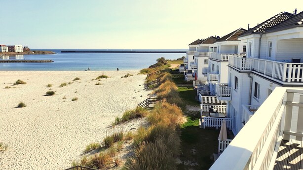A beachfront hotel with multiple balconies, a sandy beach, and a pier in the background. - Doppelhaushalfte, Ostseeresort Olpenitz (Kappeln)