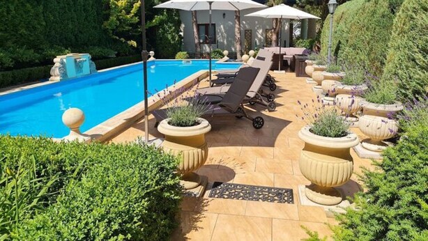 Ein Poolbereich mit Liegestühlen, Sonnenschirmen und Topfpflanzen.