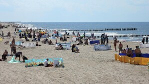 Ein belebter Strand voller Menschen, Sonnenschirme und Liegestühle.