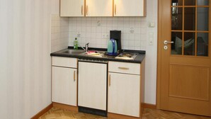 A compact kitchen with white cabinets, a black countertop, and a wooden door with a glass panel. - Wohnung in Tanne mit Einem Gemeinsamen Pool (Oberharz am Brocken)