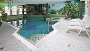 An indoor swimming pool with clear water, surrounded by white lounge chairs and a mural depicting a natural landscape. - Wohnung in Tanne mit Einem Gemeinsamen Pool (Oberharz am Brocken)