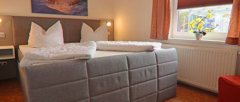 Une chambre à coucher avec un grand lit, une table de chevet, une fenêtre avec des rideaux et un tableau au mur.