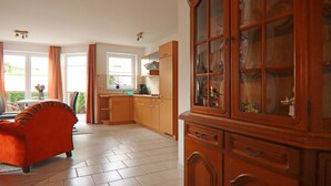 A spacious kitchen with wooden cabinets, a dining area with a red sofa, and a large cabinet with glass doors. - Appartementhaus Nicole, Zinnowitz (Zinnowitz)