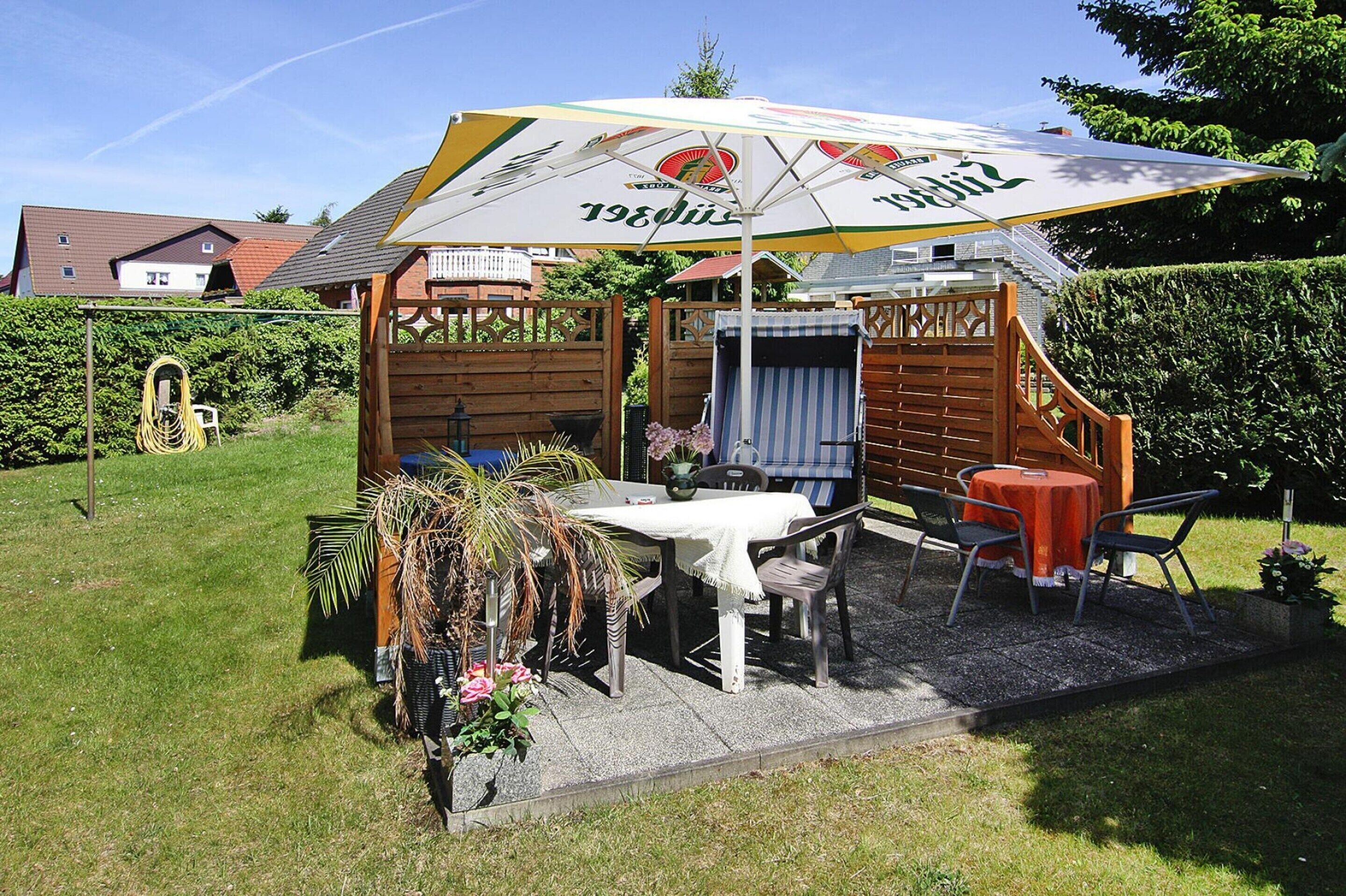 A wooden outdoor seating area with a table and chairs, an umbrella, and a small structure with a window.