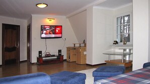 Un salon doté d’un téléviseur à écran plat fixé au mur, d’un meuble en bois et de sièges recouverts d’un tissu bleu.