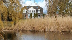 A house with a large pond in front, surrounded by tall reeds and trees. - Charmante Hausvilla in Bojendorf (Fehmarn)