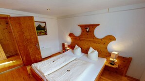 A bedroom with a wooden headboard, a large bed with white linens, two bedside tables with lamps, and a wooden floor. - Chalet in Wildkogel Near Ski Slopes (Neukirchen am Grossvenediger)