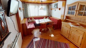 A cozy cabin interior with a wooden dining table, bench seating, a television, and a kitchen area with wooden cabinets. - Chalet in Wildkogel Near Ski Slopes (Neukirchen am Grossvenediger)