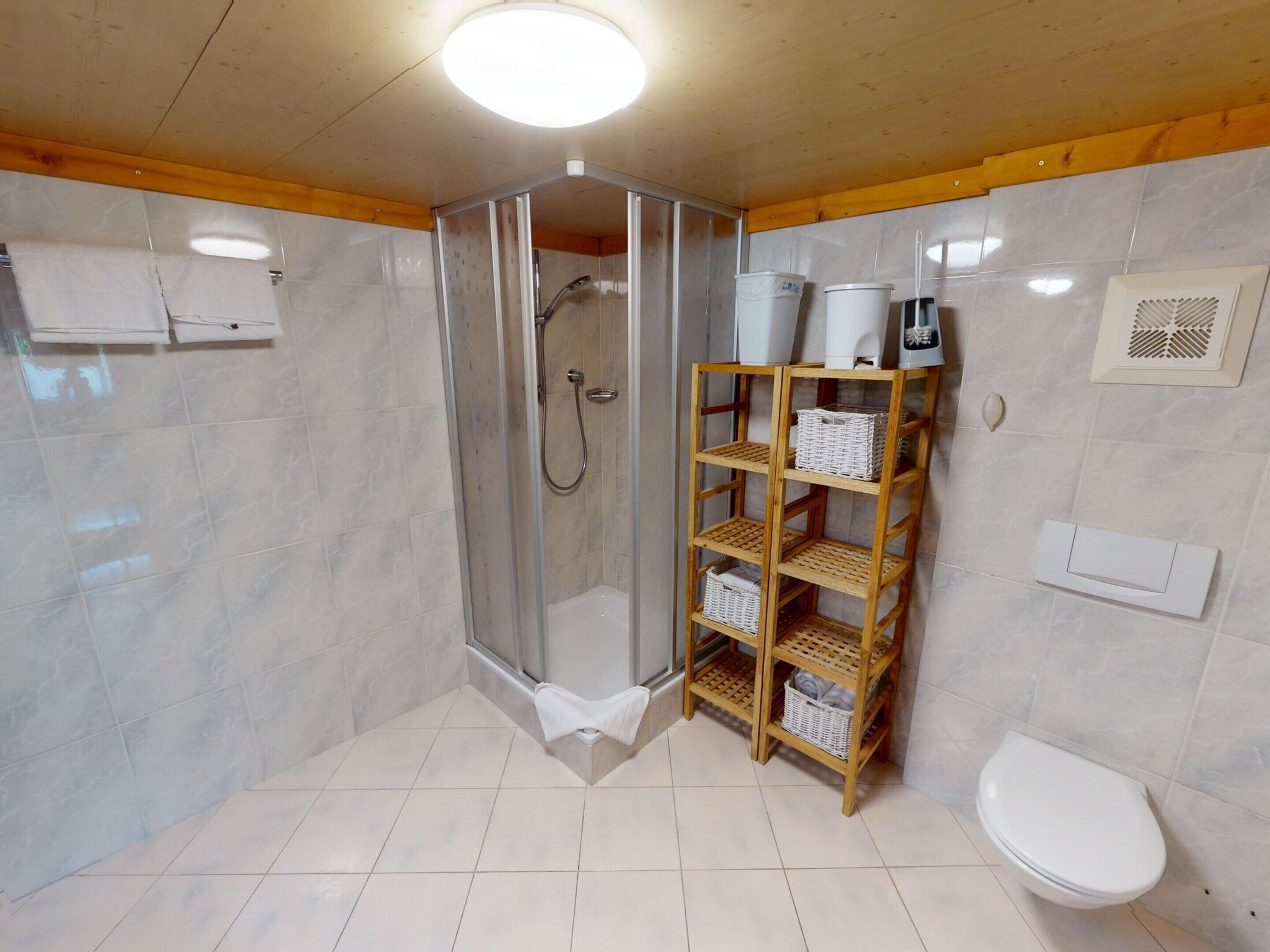 Un baño con ducha de vidrio, inodoro blanco y repisa de madera con cestas.