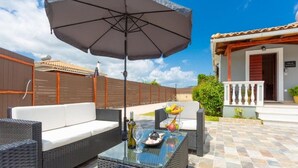 An outdoor patio with wicker furniture, a glass table, and a large umbrella. - Villa Mansion With Private Pool (Zakynthos)