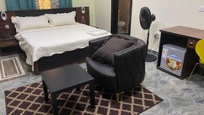 A bedroom with a bed, a small table, a massage chair, a desk with a fan, and a minibar. - Prodis Hotel and Suites (Sagamu)