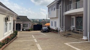 A residential area with a paved driveway, a car parked in the driveway, and a building with a balcony. - Prodis Hotel and Suites (Sagamu)