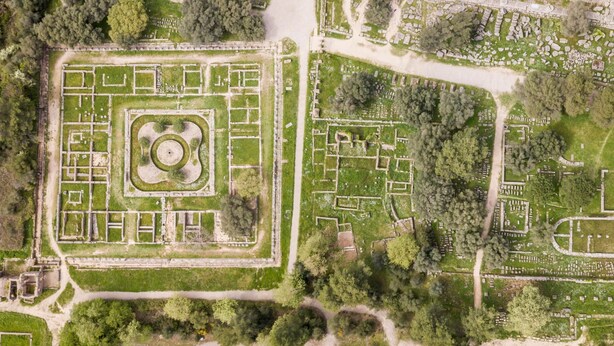 An aerial view of a large, well-maintained park with distinct geometric pathways and a central circular area, surrounded by various smaller landscaped sections. - Yiannis Maizonette Ancient Olympia (Archaia Olympia)