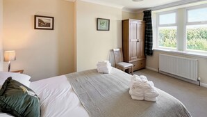 A hotel room with a bed, a chair, a wardrobe, and a window with a view of greenery. - 2 bedroom accommodation in Castle Douglas (Castle Douglas)