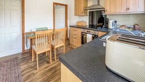 A compact kitchen with wooden cabinets, a built-in oven, a stainless steel range hood, and a granite countertop. - 2 bedroom accommodation in Castle Douglas (Castle Douglas)