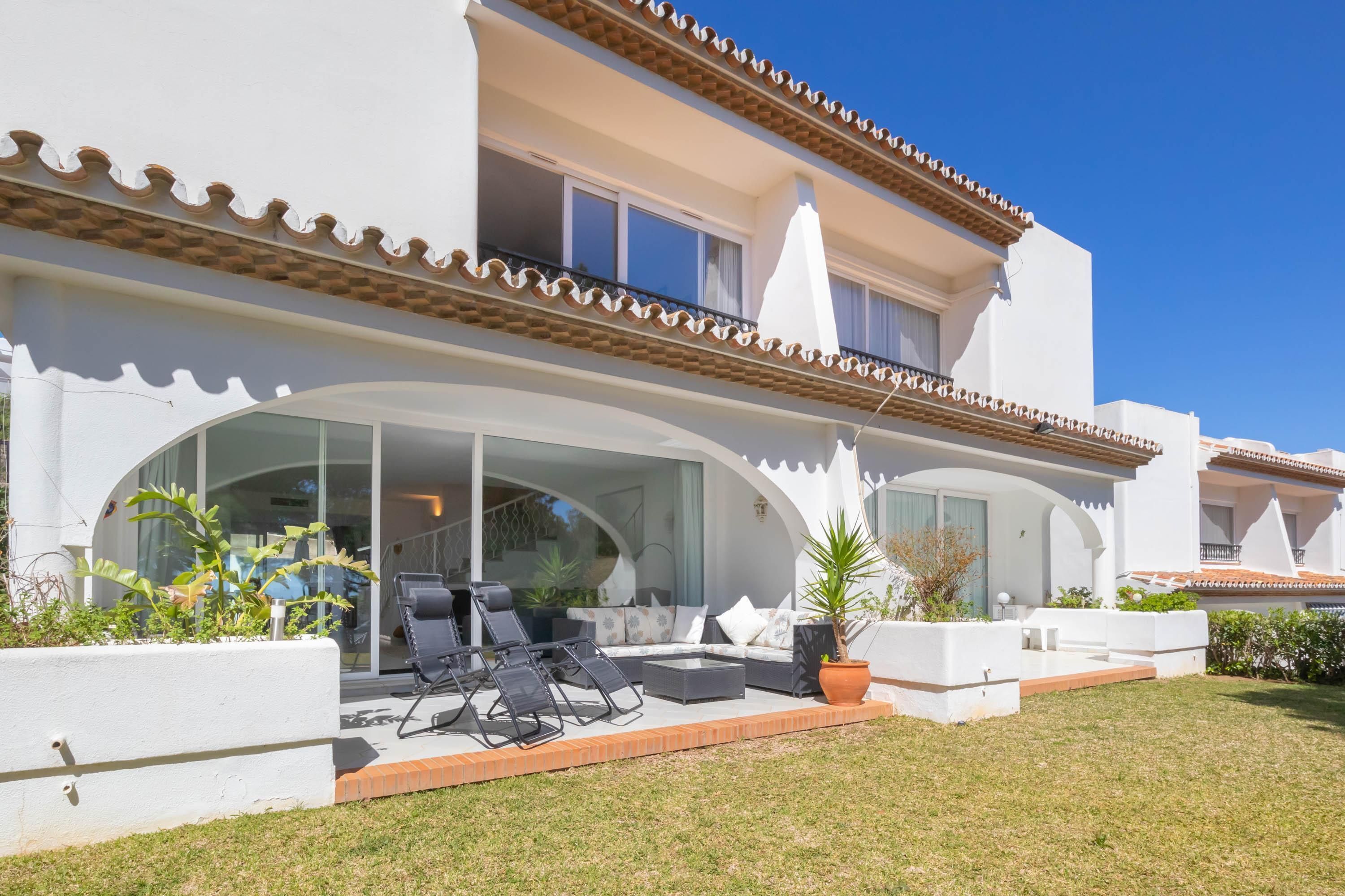A two-story house with a patio area featuring outdoor furniture and potted plants.