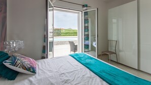 A bedroom with a bed, a chair, a wardrobe, and a sliding glass door leading to an outdoor area.
