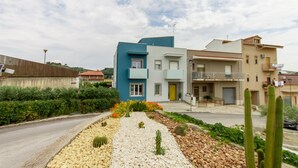 A modern two-story house with a blue and white facade, a small balcony, and a garden with cacti and flowers.