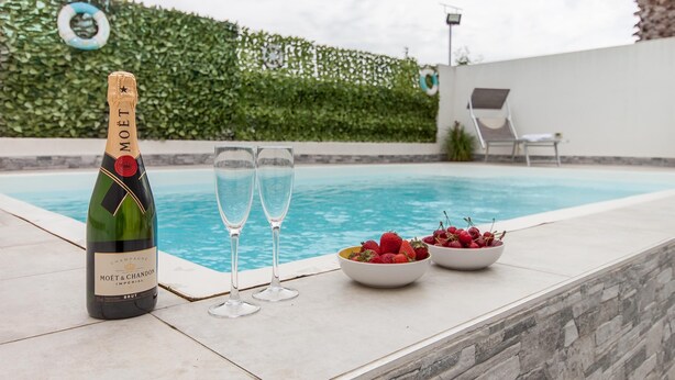 A bottle of Moët & Chandon champagne, two glasses, and a bowl of strawberries by a pool.