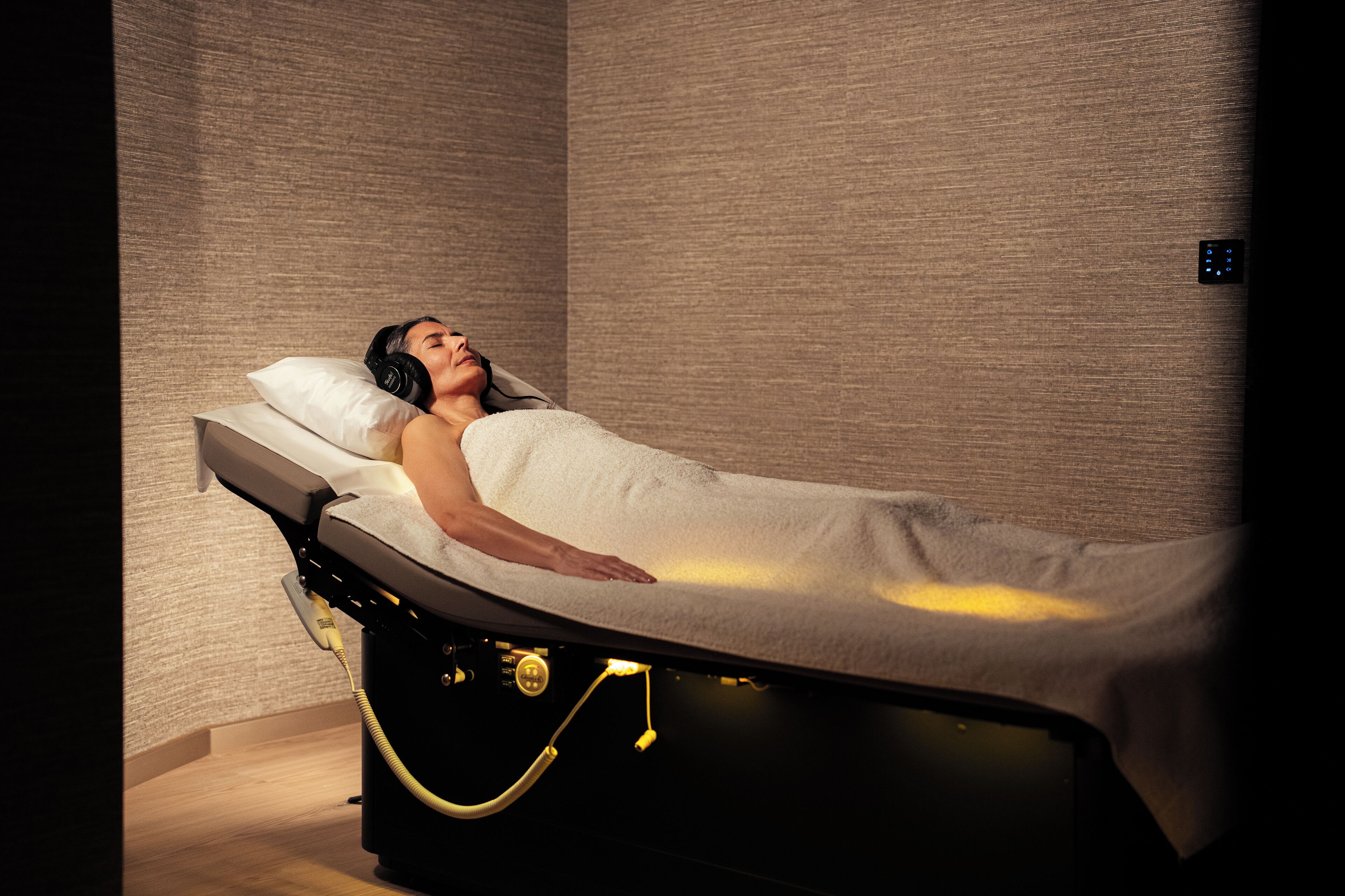 Ein Massageraum mit Liege, Bedienfeld und einer Massagevorrichtung an der Wand.