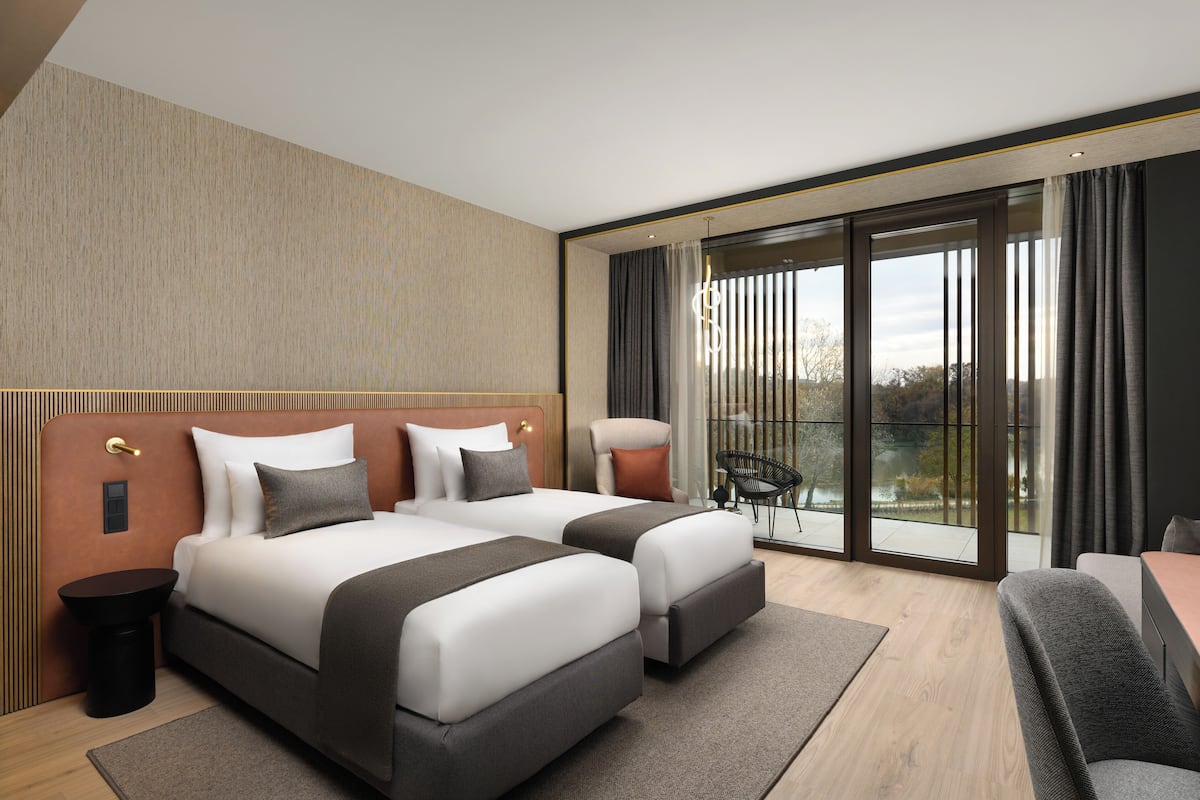 A modern hotel room with two beds, a dining area, and a balcony with a view.