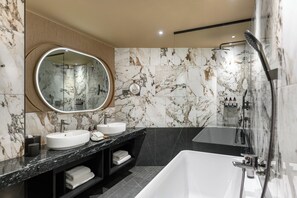 Un baño moderno con un espejo ovalado grande, dos lavamanos, una bañera y una ducha.