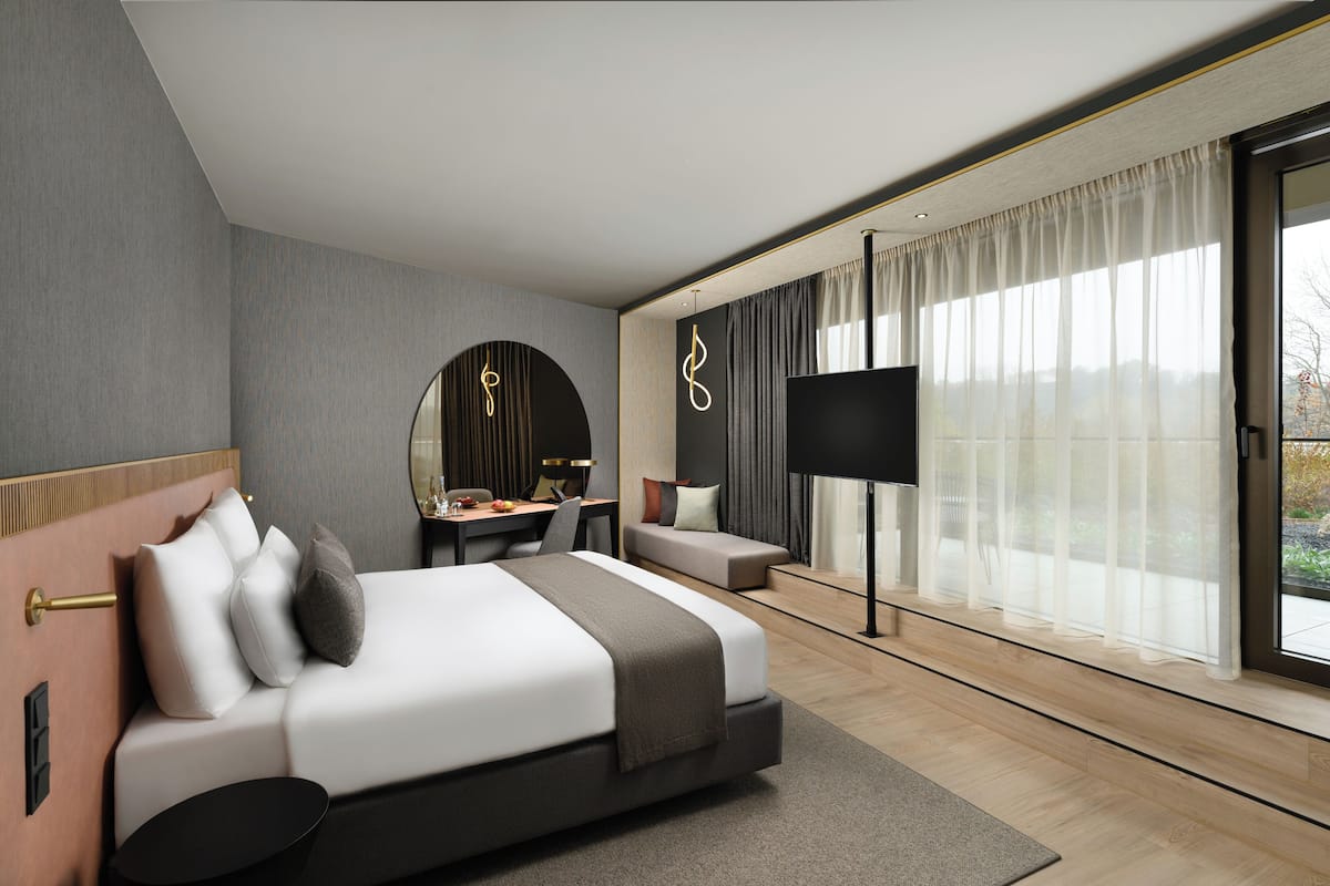 A modern hotel room with a large bed, a desk, a sofa, and a TV.