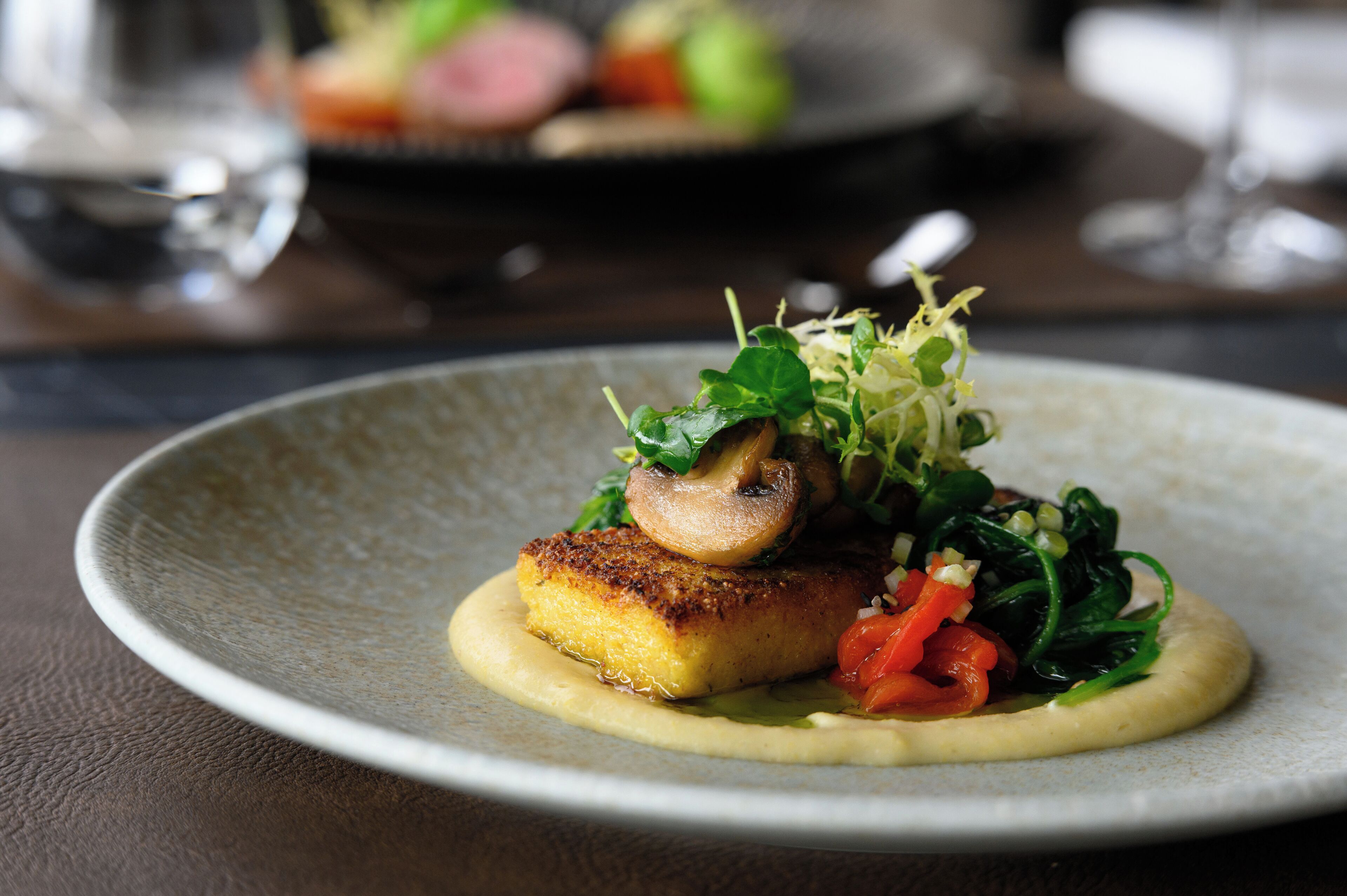 Une assiette de nourriture comprenant un morceau de poisson, des champignons, des légumes verts et une cuillerée de sauce.