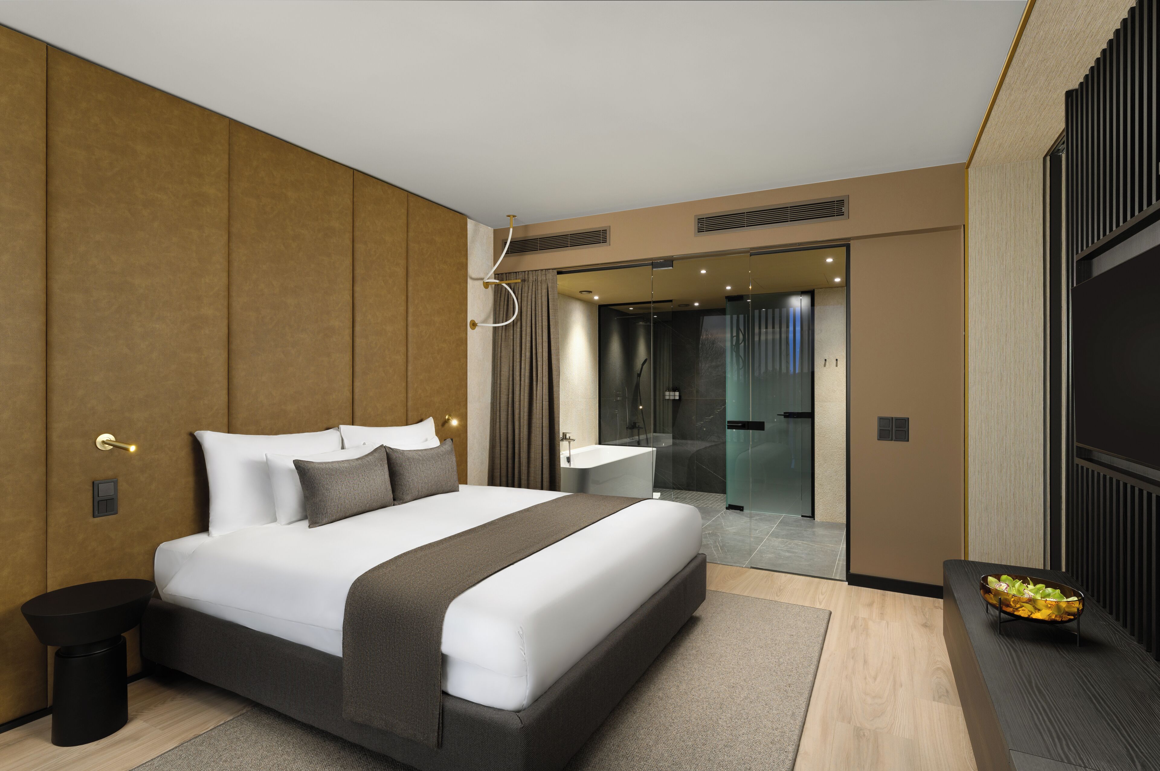 A modern hotel room with a large bed, a bathroom with a bathtub, and a seating area with a bowl of fruit.