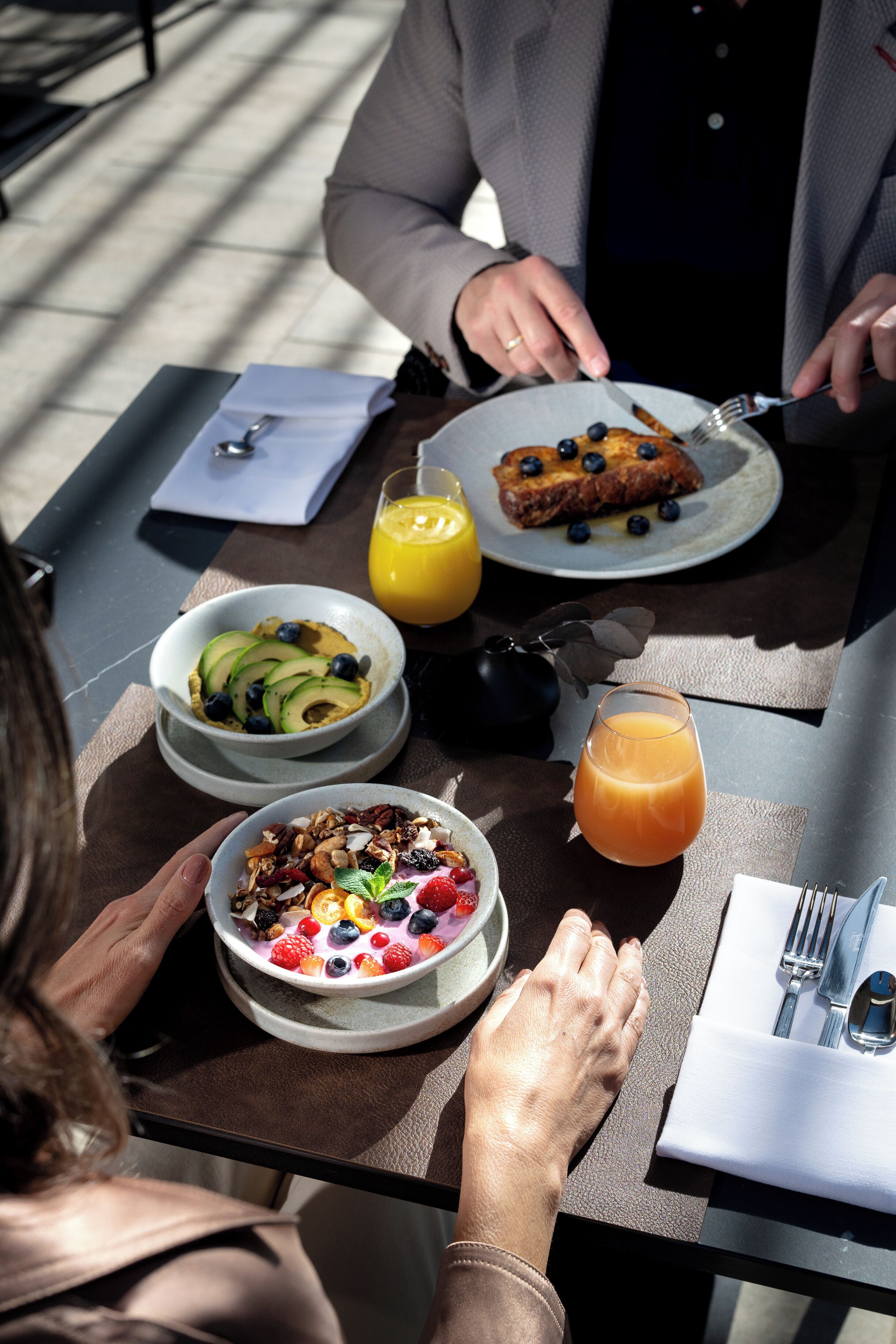 A breakfast setting with a table set for two, featuring plates of food, a bowl of fruit, and a glass of orange juice.