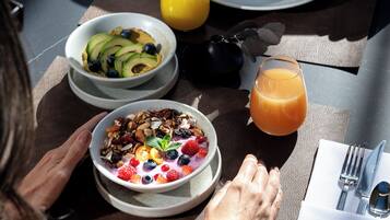 A breakfast setting with a table set for two, featuring plates of food, a bowl of fruit, and a glass of orange juice.