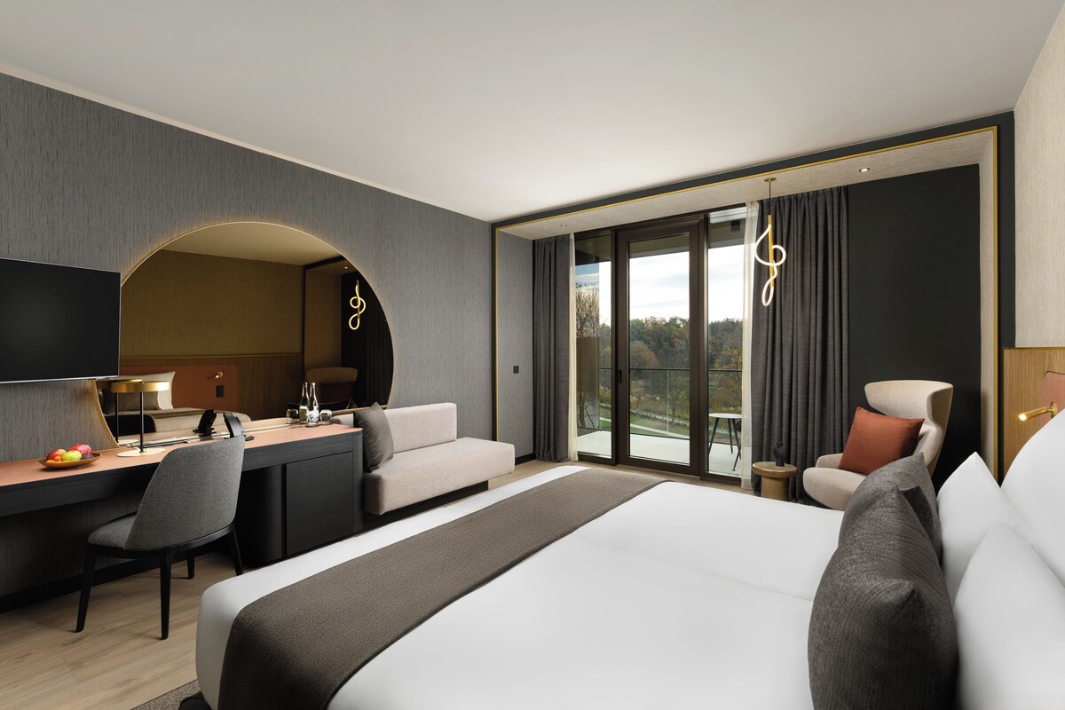 A modern hotel room with a large bed, a desk, a sofa, and a TV.