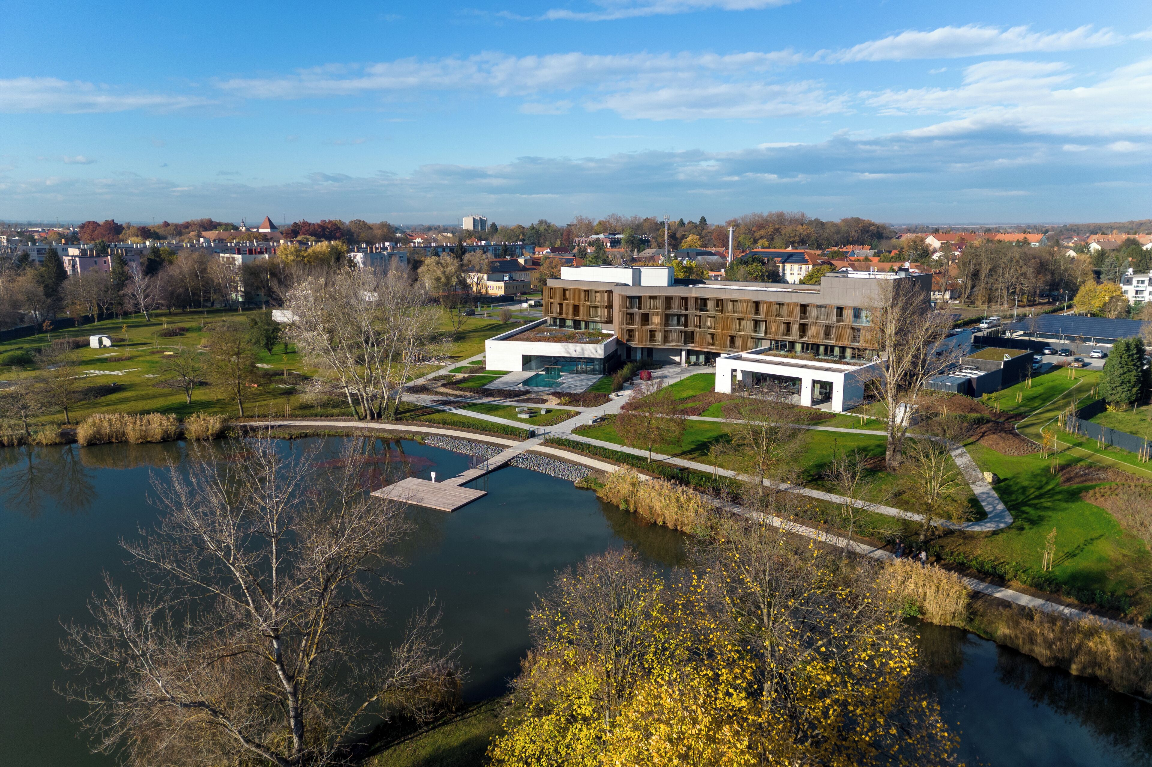 Ein moderner Gebäudekomplex mit einem zentralen Innenhof, einer Brücke über dem Wasser und umliegender Bepflanzung.