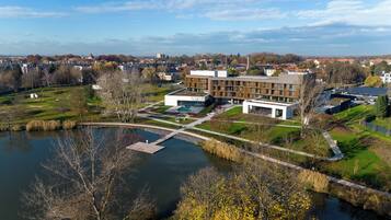 Ein moderner Gebäudekomplex mit einem zentralen Innenhof, einer Brücke über dem Wasser und umliegender Bepflanzung.