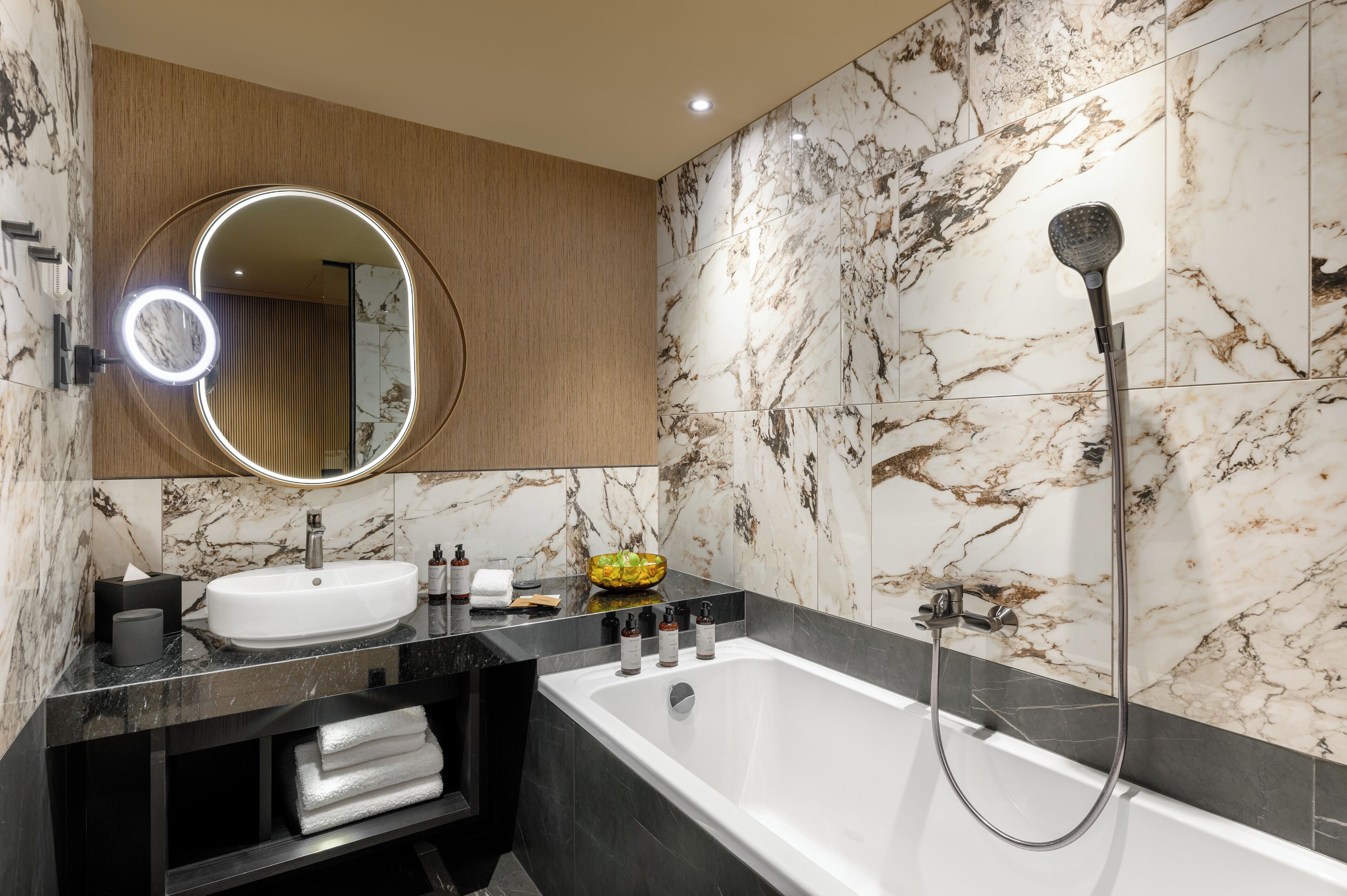 Een moderne badkamer met een marmeren wastafelmeubel, een grote spiegel met ingebouwde verlichting, een badkuip en een handdouche.
