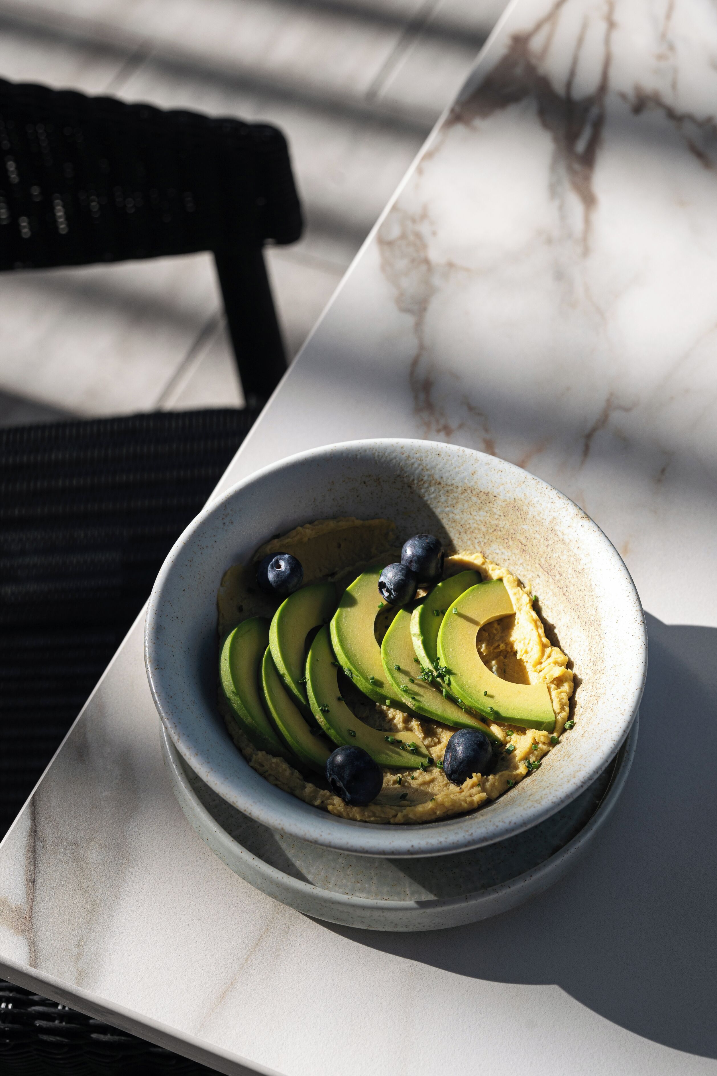 A bowl of avocado and blueberry salad on a marble table.