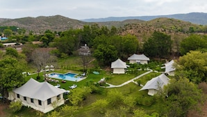 Un resort con varias tiendas blancas, una piscina y abundante vegetación.
