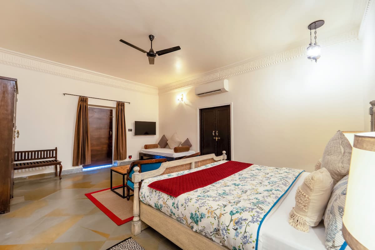 A bedroom with a bed, a desk, a chair, a bench, a ceiling fan, and an air conditioning unit.