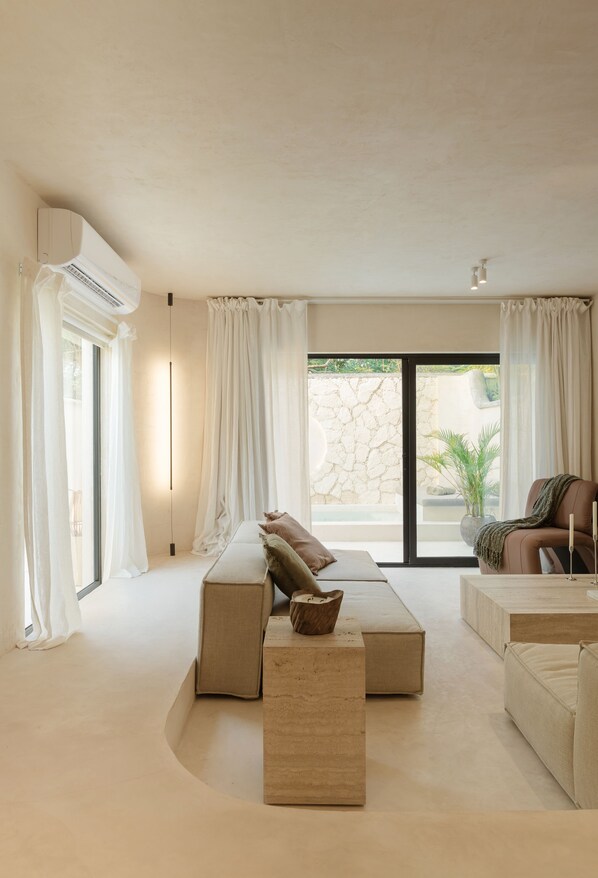 A modern living room with a large sectional sofa, a coffee table, and a view of a stone wall and greenery outside.