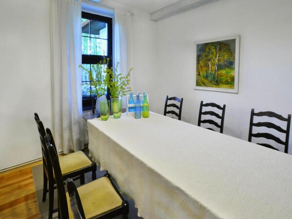 A dining room with a long table, chairs, a window with curtains, and a painting on the wall.