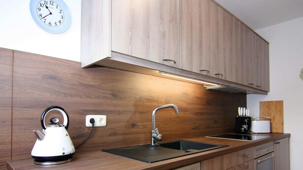 Eine moderne Küche mit Holzausstattung, einem Edelstahl-Wasserkocher, einer Spüle und einer Uhr an der Wand.