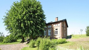 Ett traditionellt hus byggt av tegel, med ett stort träd framför, omgivet av välskött gräsmatta och buskar.