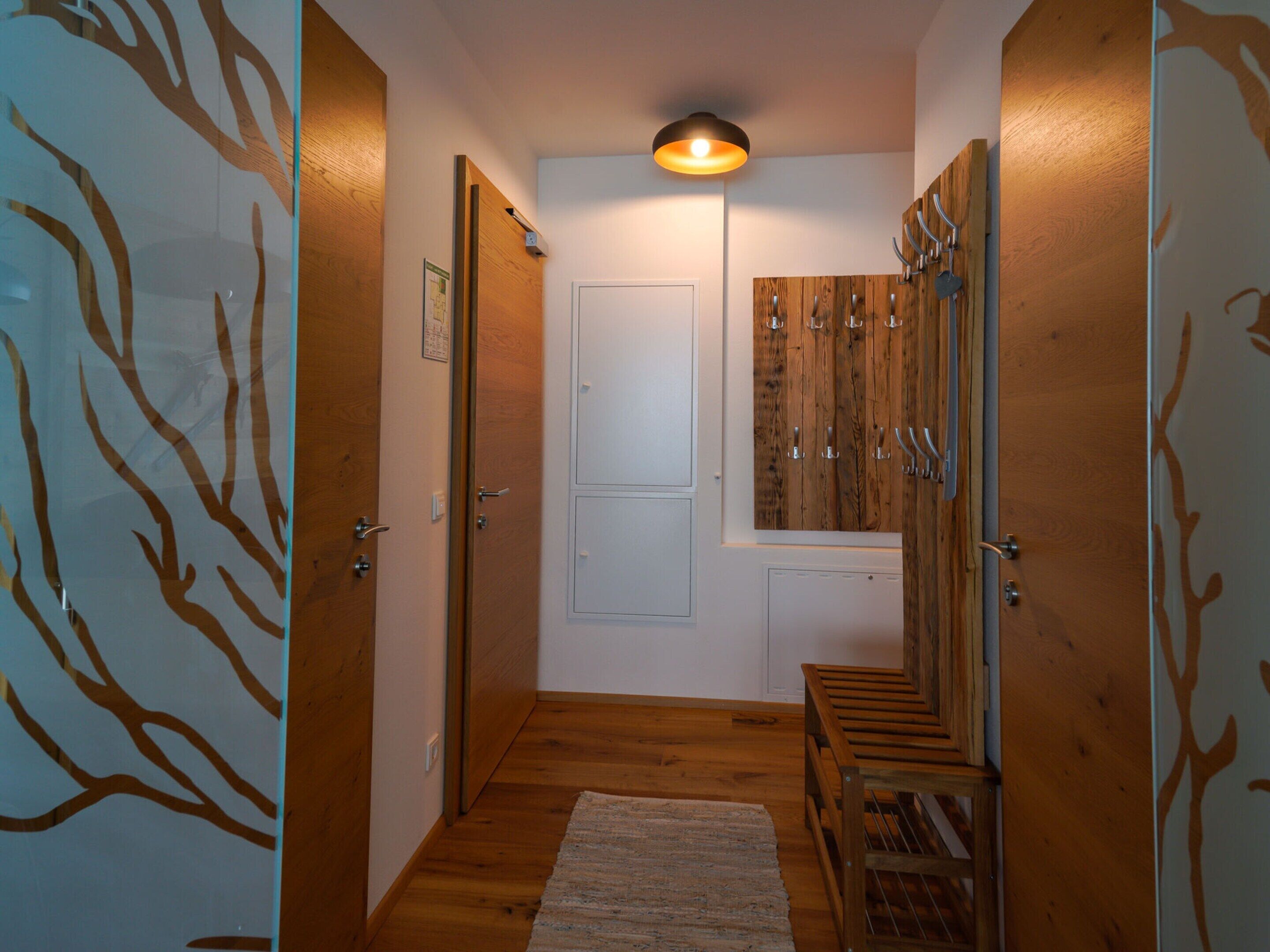 A hallway with wooden floors, a white door, and a coat rack.