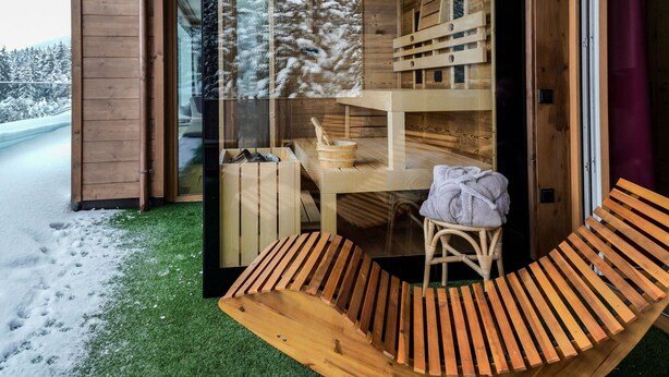 Une cabane en bois avec une porte en verre, un banc en bois et une petite table sur laquelle est posée une serviette.
